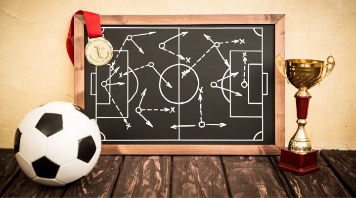 A blackboard containing a diagram of a soccer formation flanked by a soccer ball and a trophy