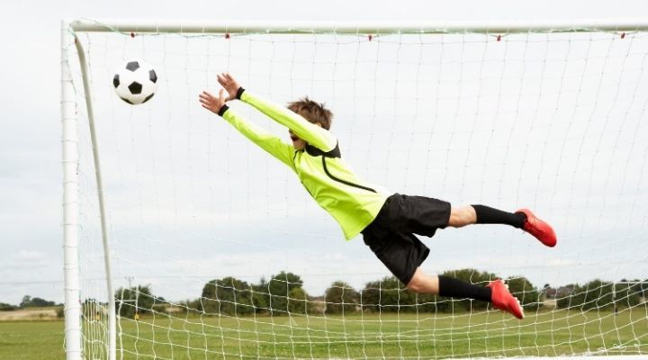 A young goalkeeper in yellow jumping to catch the ball
